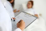 A doctor writing on a clipboard while talking to someone.