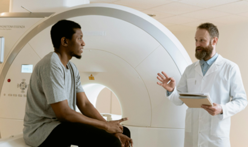 A man talking to another man in front of an mri machine.