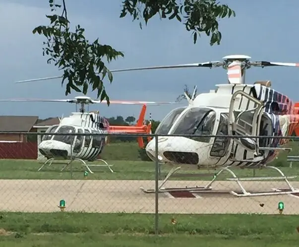 Two white helicopters are parked on the ground.