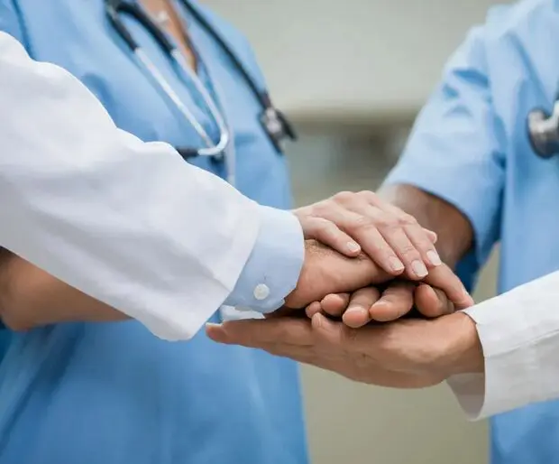 A group of doctors holding hands in the middle of a hospital.