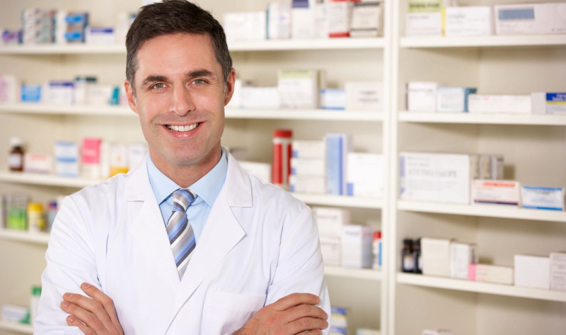 A man in white lab coat standing next to shelves.